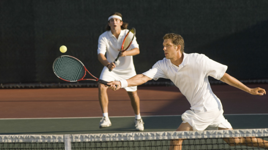 Young male tennis player hitting ball with doubles partner standing in background