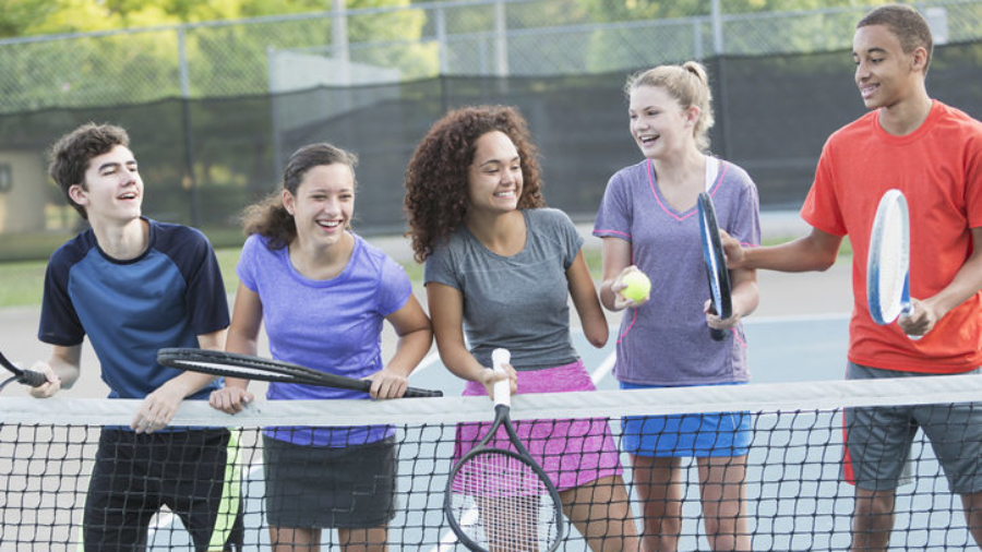 Multi-ethnic teenagers playing tennis.  Girl in middle (17 years, mixed race) is a physically challenged amputee.