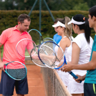 Coach teaching tennis lessons to a group of people and helping them hold the racket properly - outdoors sports concepts